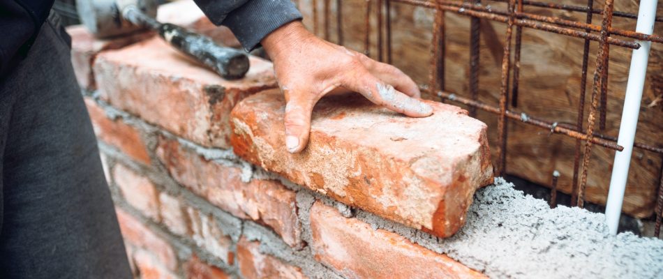 Bricklayer worker installing brick masonry on exterior wall with hands and tools