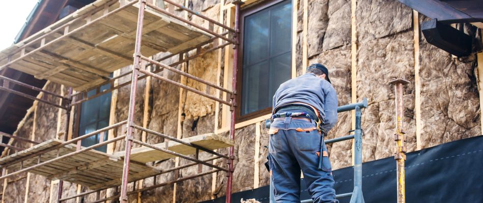 Construction worker thermally insulating house facade with glass wool.